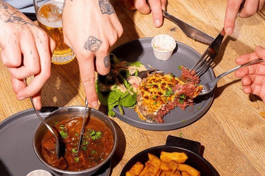 A meal with a plate of food, a bowl of sauce, and a glass of beer on a wooden table. 1