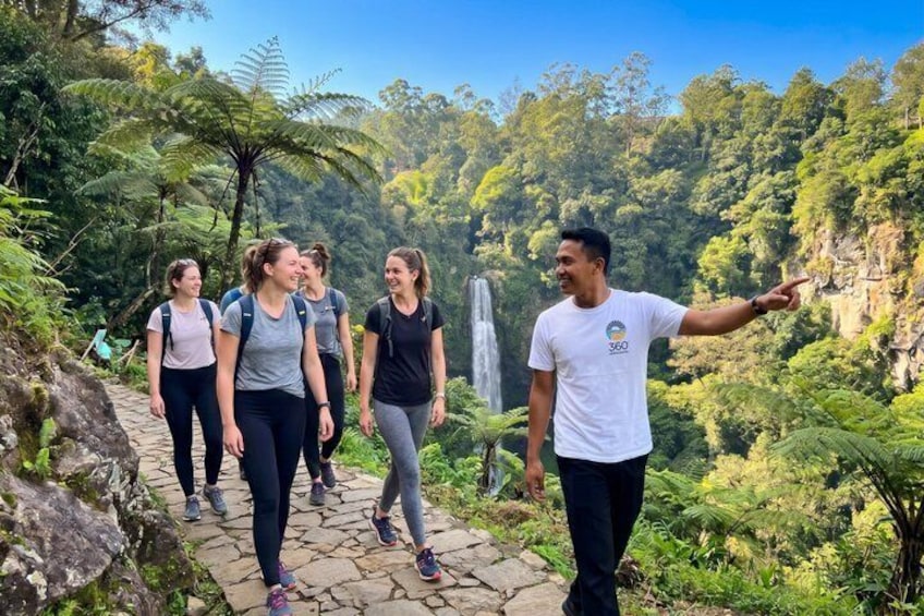 A group of people hiking on a stone path surrounded by lush greenery and a waterfall. 1