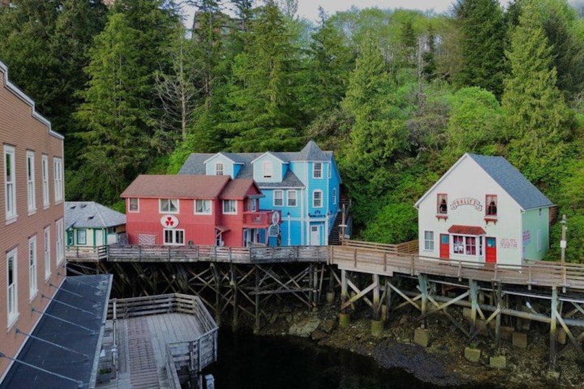 A waterfront with colorful buildings, a wooden pier, and dense forest in the background. 2