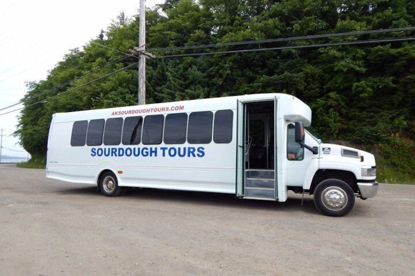 A white tour bus with 'Sourdough Tours' branding parked on a road with trees in the background. 2
