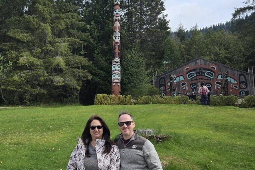 A totem pole and a building with indigenous art in a forested area. 4