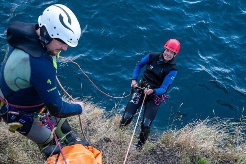 Two people rappelling down a cliff with ocean in the background. 5