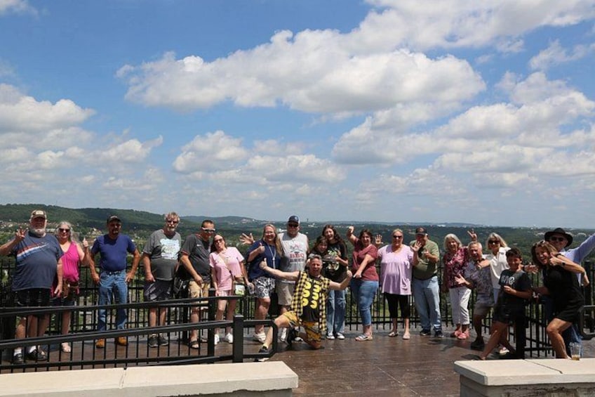 A group of people standing on a platform with a scenic view of hills and a partly cloudy sky. 4