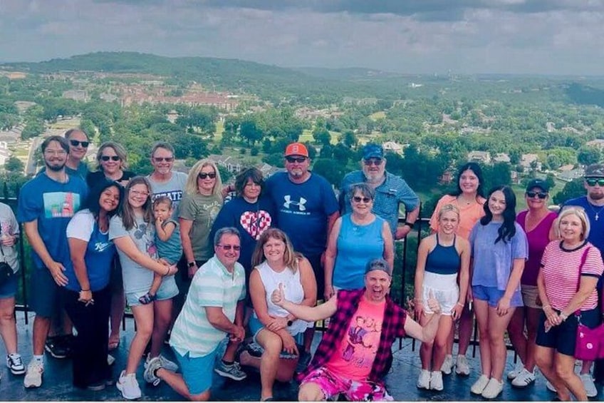 A group of people posing for a photo on a hill overlooking a landscape with houses and greenery. 3