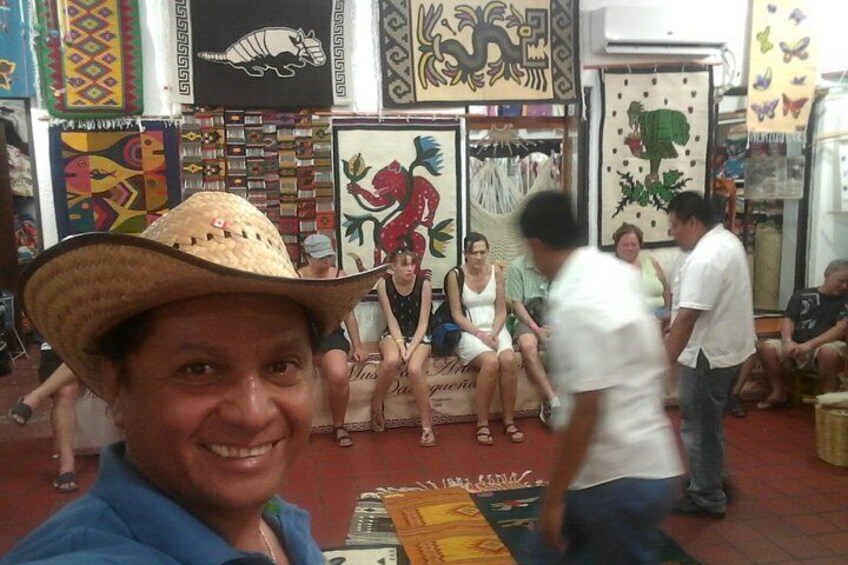 A man in a straw hat, a woman in a white dress, and several people sitting and standing in a room with colorful decorations and textiles. 3