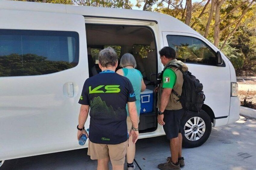 A white van with its door open, people standing beside it, and a backpack on the ground. 2