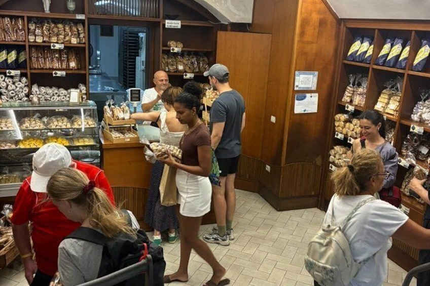 A bakery with shelves of baked goods and people shopping. 4