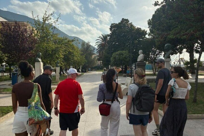 A group of people walking along a paved path in a park with trees and statues. 2