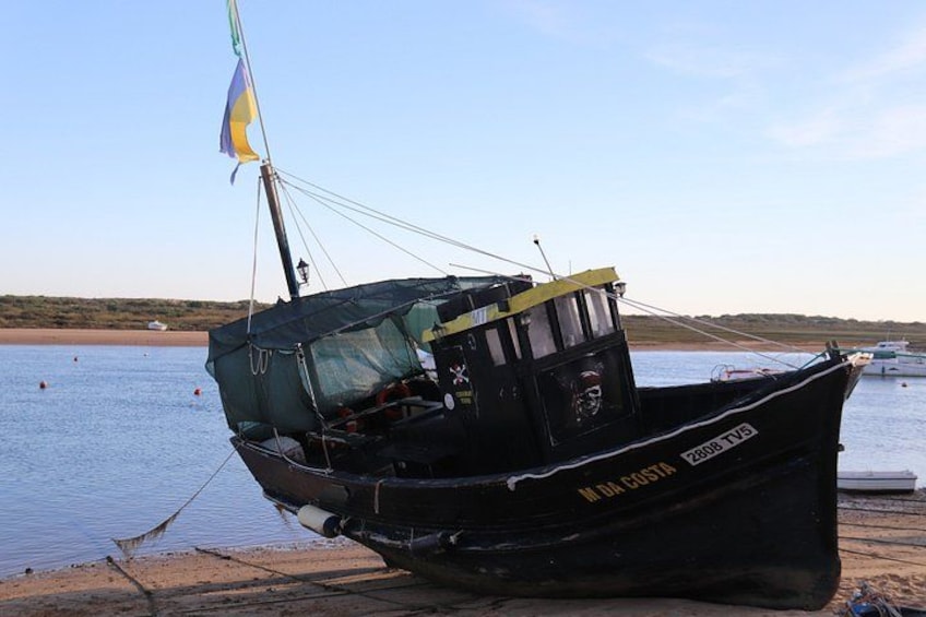 A black boat with a flag, docked at a sandy beach with calm water and a clear sky. 5