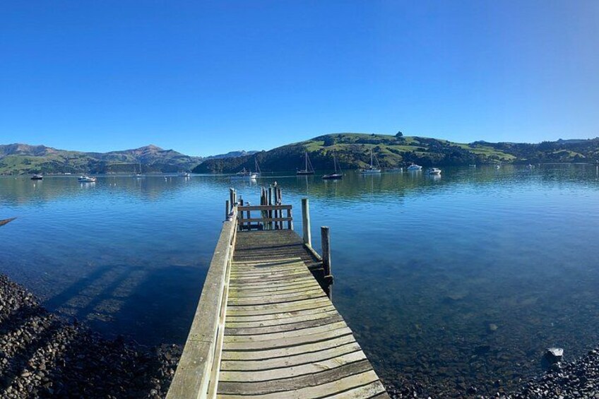 A wooden pier extending into calm water, surrounded by hills and boats in the distance. 4