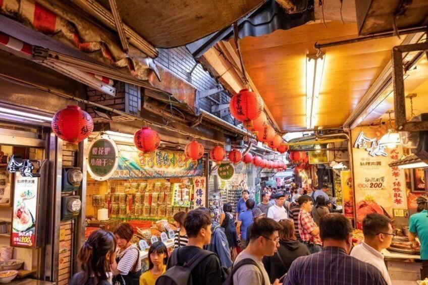 A bustling street market with red lanterns, various shops, and people shopping. 4