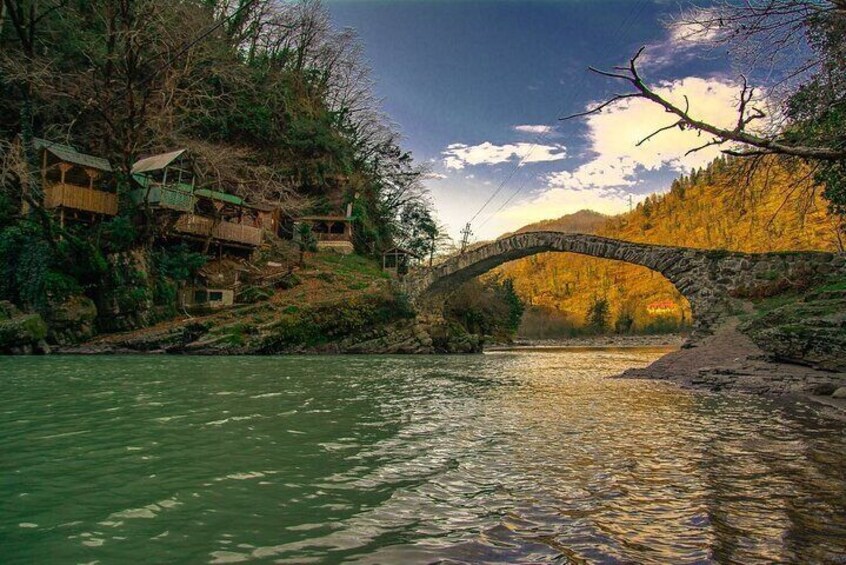 A stone bridge over a river, surrounded by autumn-colored trees and wooden houses. 5