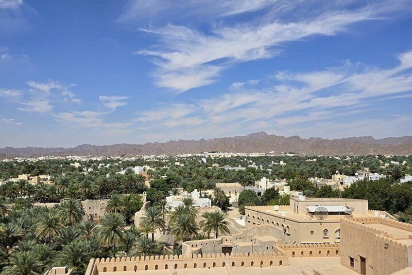 A cityscape with palm trees, buildings, and distant mountains under a clear sky. 2