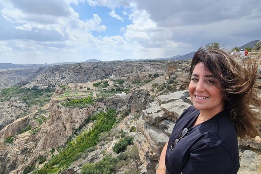 A person standing on a rocky outcrop overlooking a terraced landscape with greenery and distant hills. 1