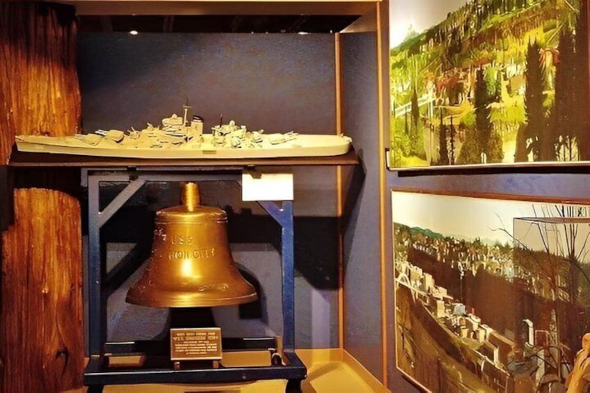 A model ship on a display stand, a bell, and two framed photographs. 3