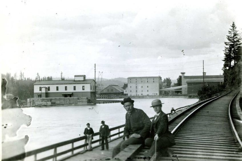 A train track with a bridge, buildings, and a body of water. 4