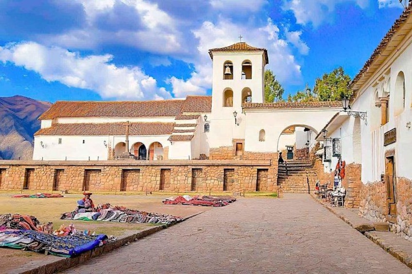 A plaza with a white church, a bell tower, and a stone wall. 1