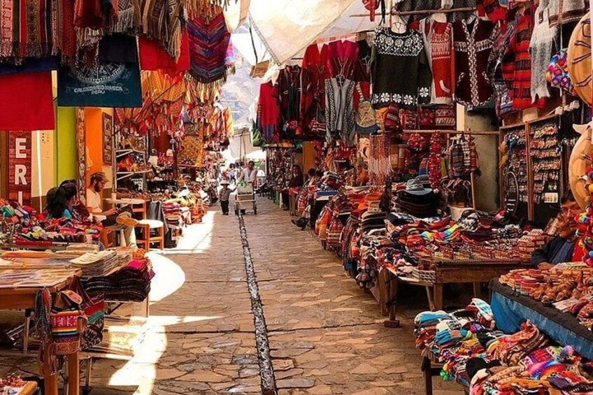 A bustling market with colorful textiles and handicrafts displayed on tables and hanging from the ceiling. 2