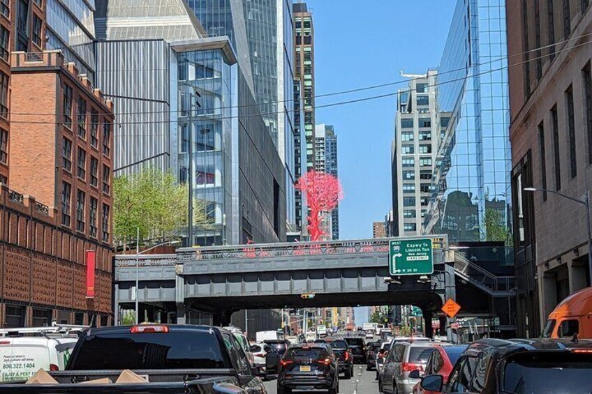 A busy urban street with tall buildings, a pedestrian bridge, and a red sculpture. 2
