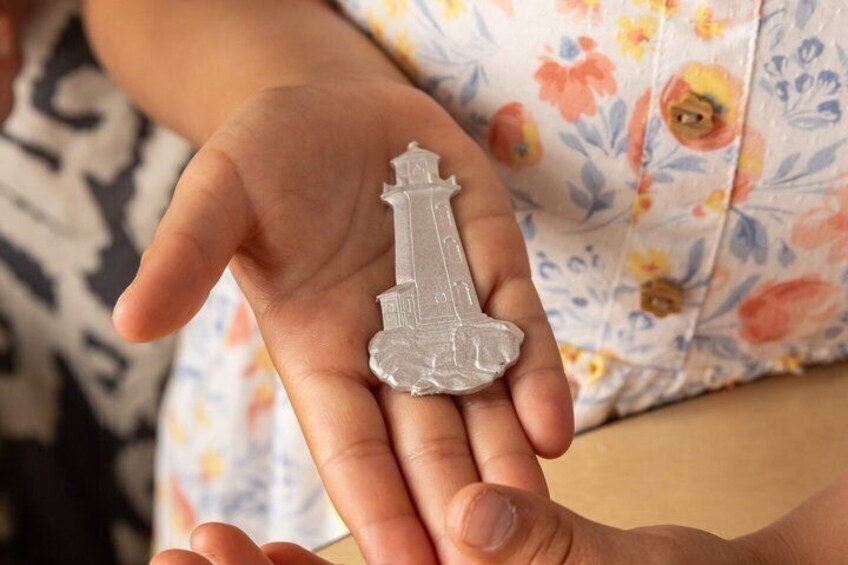 A hand holding a small, clear, transparent model of a lighthouse. 4