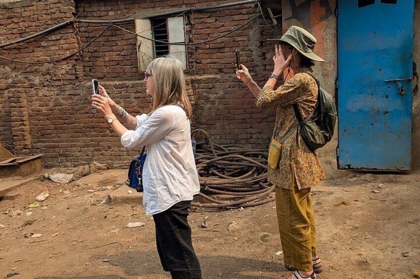 Two people taking photos with smartphones in an outdoor setting with a brick wall and a blue door in the background. 4