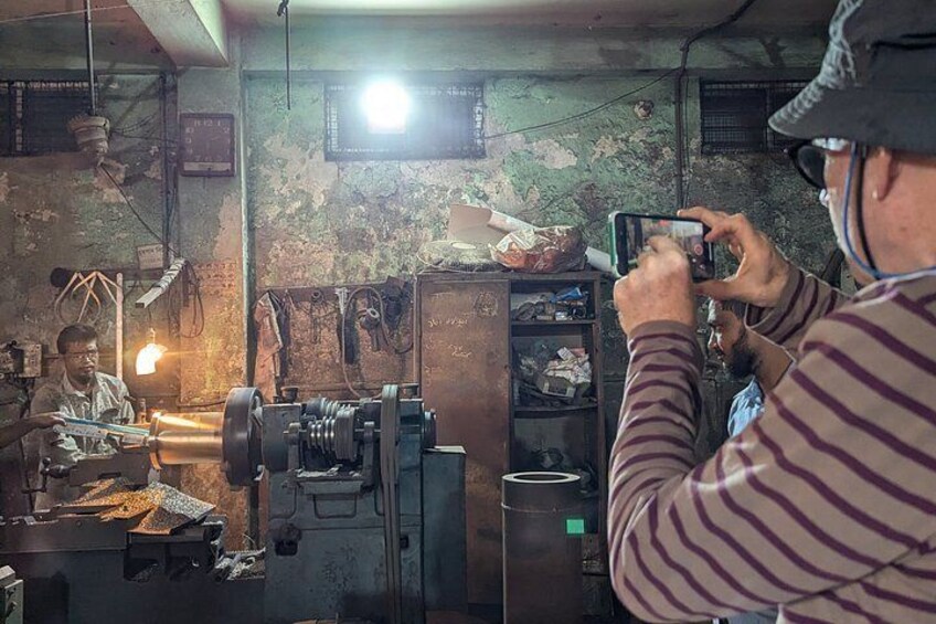 A workshop with machinery, a person operating a lathe, and another person taking a photo. 5