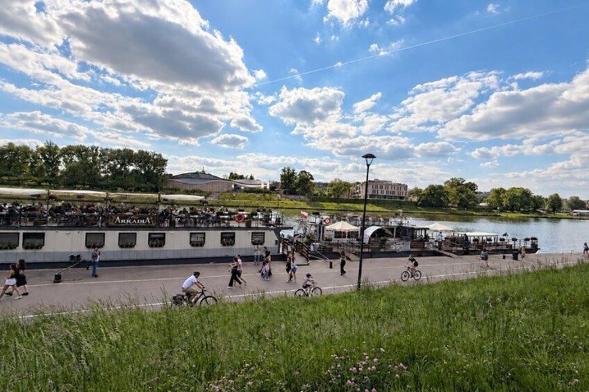 A riverside scene with a boat, people walking, and bicycles. 2