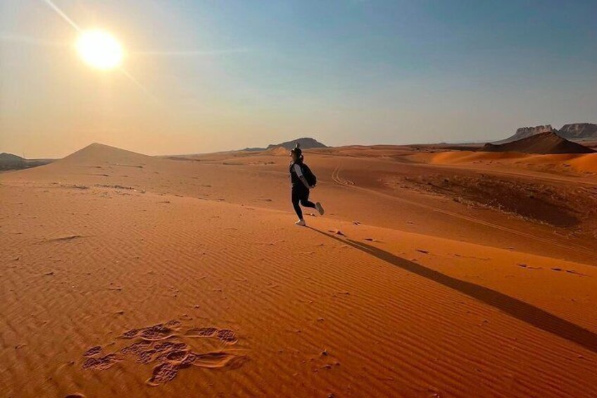 A person running on a desert sand dune with a clear sky and sun in the background. 2