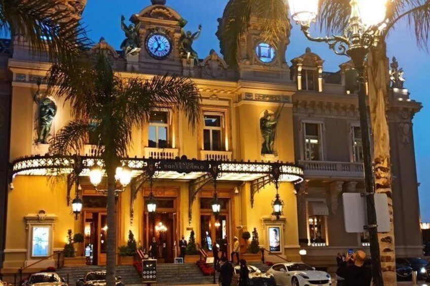 A grand building with a clock tower, ornate balconies, and a well-lit entrance. 1