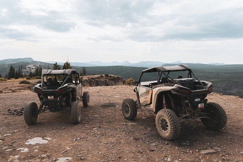 Two off-road vehicles parked on a dirt road with a mountainous landscape in the background. 5