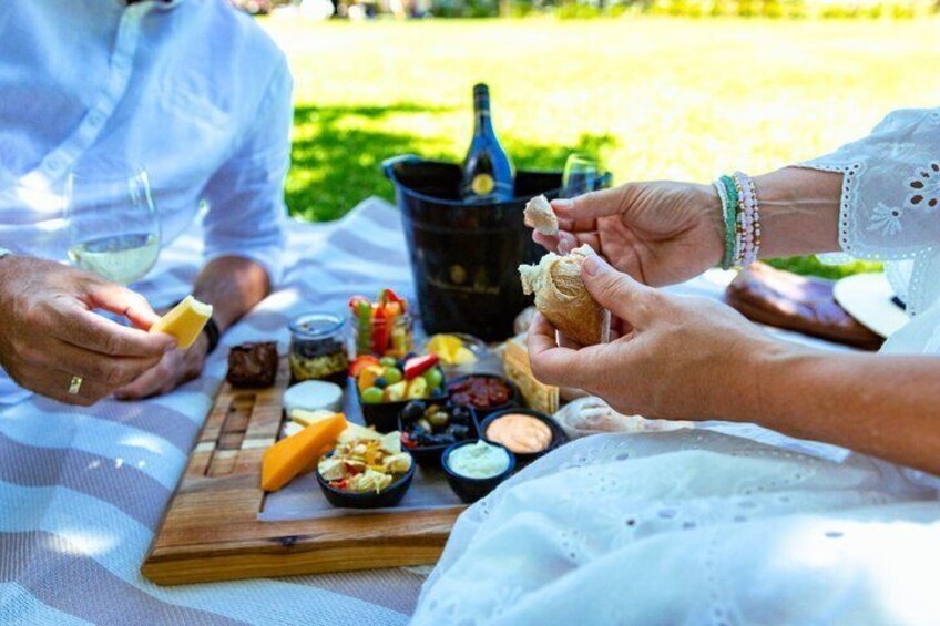 A picnic with a wooden board, cheese, bread, and various spreads. 1