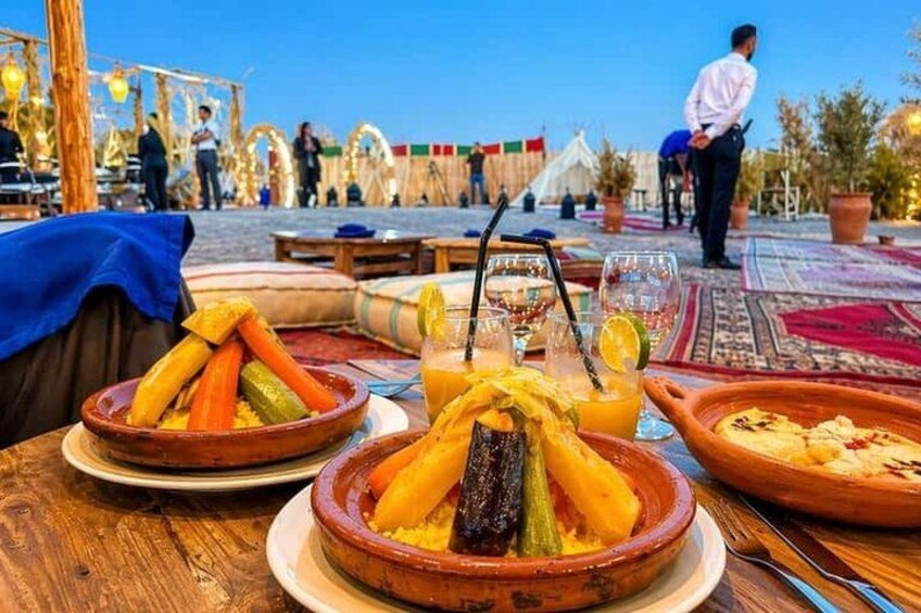 A dining table with traditional Moroccan dishes, a drink with a straw, and a tent in the background. 3
