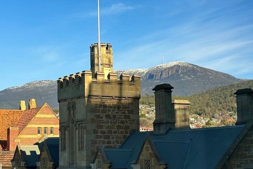 A stone building with a flagpole, surrounded by houses with red roofs, and a mountain in the background. 2