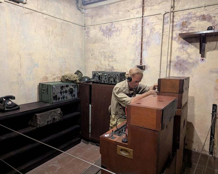 A person working with vintage electronic equipment in a room with worn walls and a metal shelf. 3
