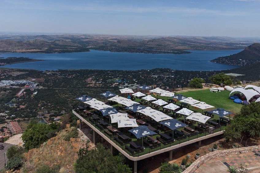 A camping area with tents and canopies, a lake, and a hilly landscape in the background. 1