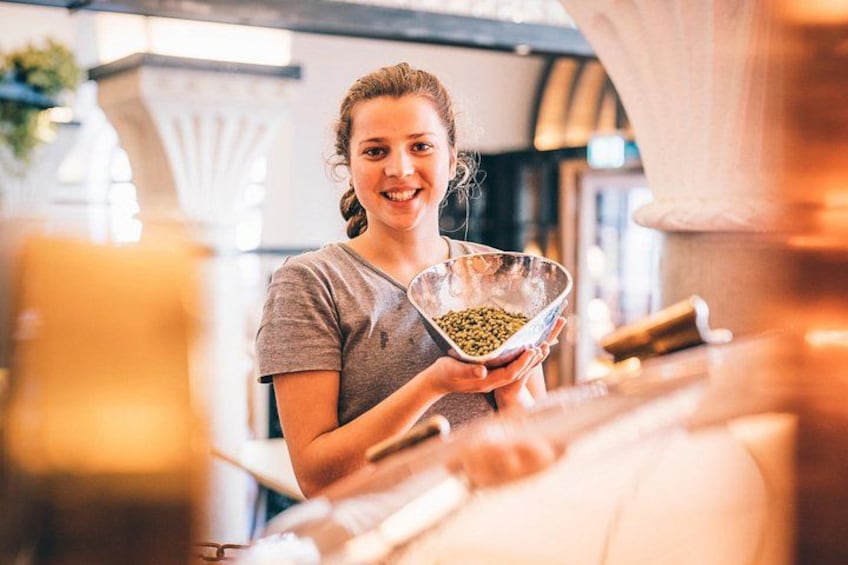 A person holding a metal bowl with green contents, in a kitchen setting with a large pot and a window in the background. 5