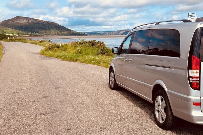 A silver van parked on a road with a sign reading 'PASSING PLACE' on the back. 1