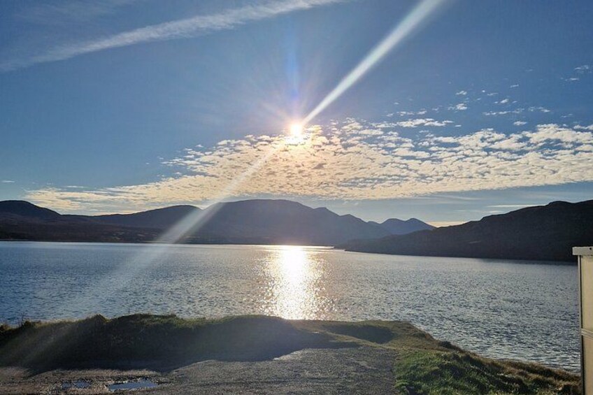 A lake with mountains in the background and the sun setting over the horizon. 3
