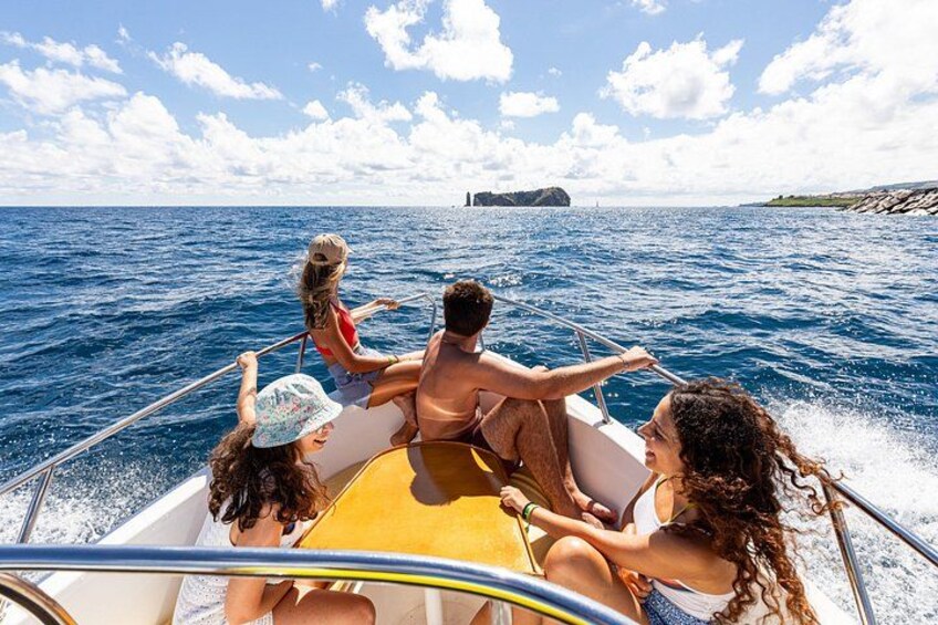 A group of people on a boat in the ocean, with a rocky coastline in the background. 5