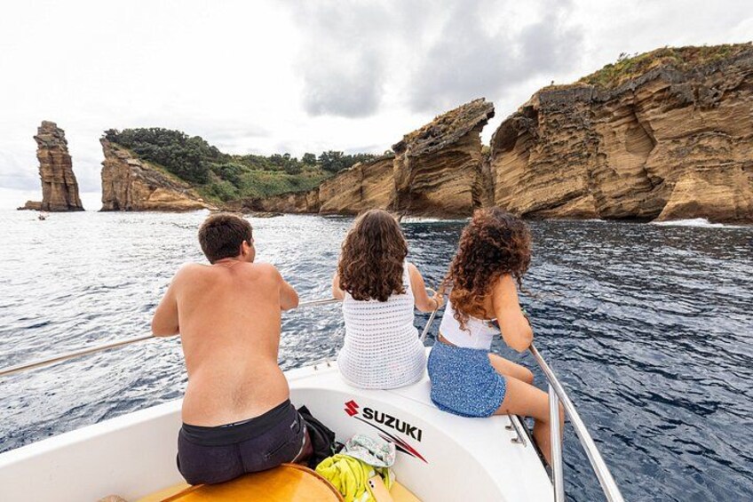 Three people on a boat with a rocky coastline in the background. 2