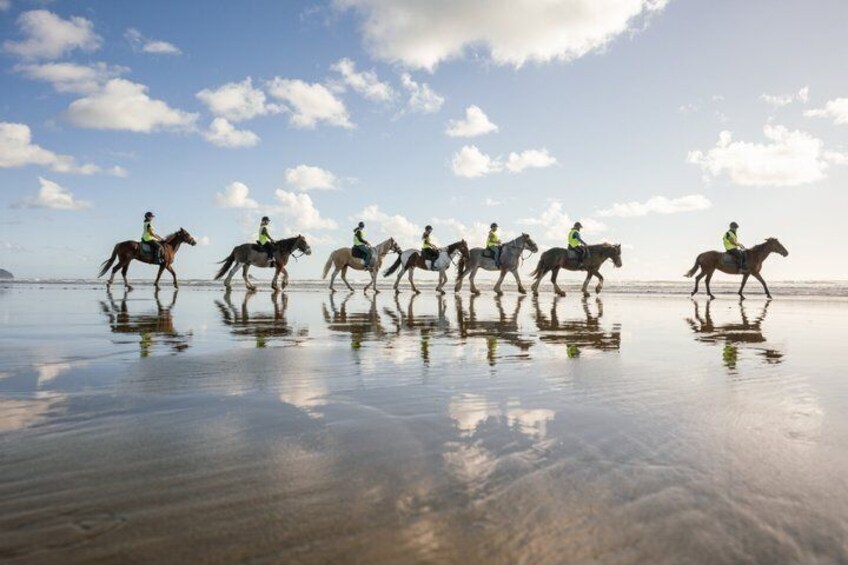 A group of people riding horses on a wet beach with reflections. 1