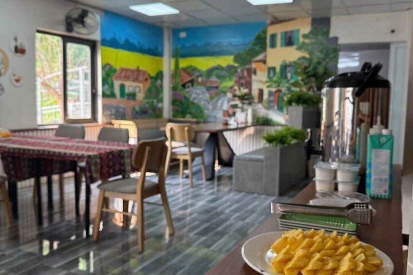 A restaurant interior with a mural, tables, chairs, a coffee machine, and a plate of food. 5