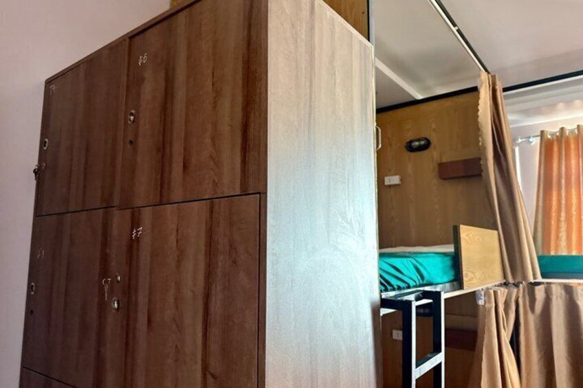 A wooden wardrobe, a bed with a blue mattress, and a curtain. 3