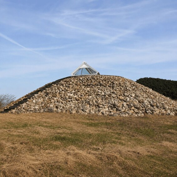 A stone pyramid with a glass pyramid structure on top, surrounded by dry grass and a clear sky. 2