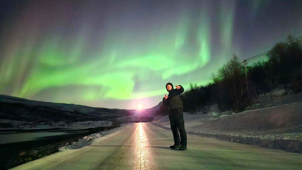 A person standing on a road with the Northern Lights in the background. 2