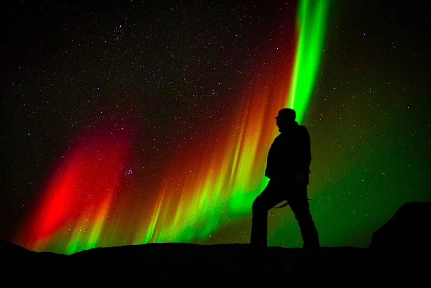 A silhouette of a person standing under a colorful aurora display. 1