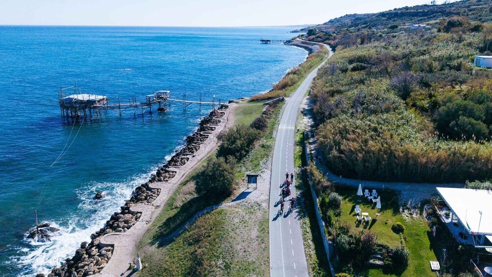 A coastal road with a rocky breakwater, a pier, and a grassy area with outdoor seating. 3