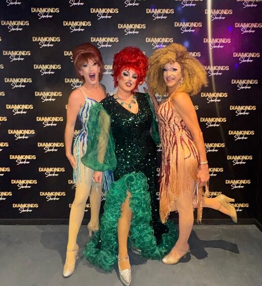Three individuals in elaborate costumes posing in front of a backdrop with repeated text. 2
