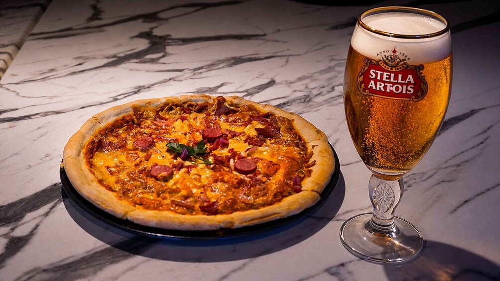 A pizza with toppings and a glass of Stella Artois beer on a marble surface. 3