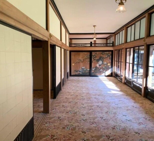 A hallway with patterned carpet, wooden beams, and large windows. 1